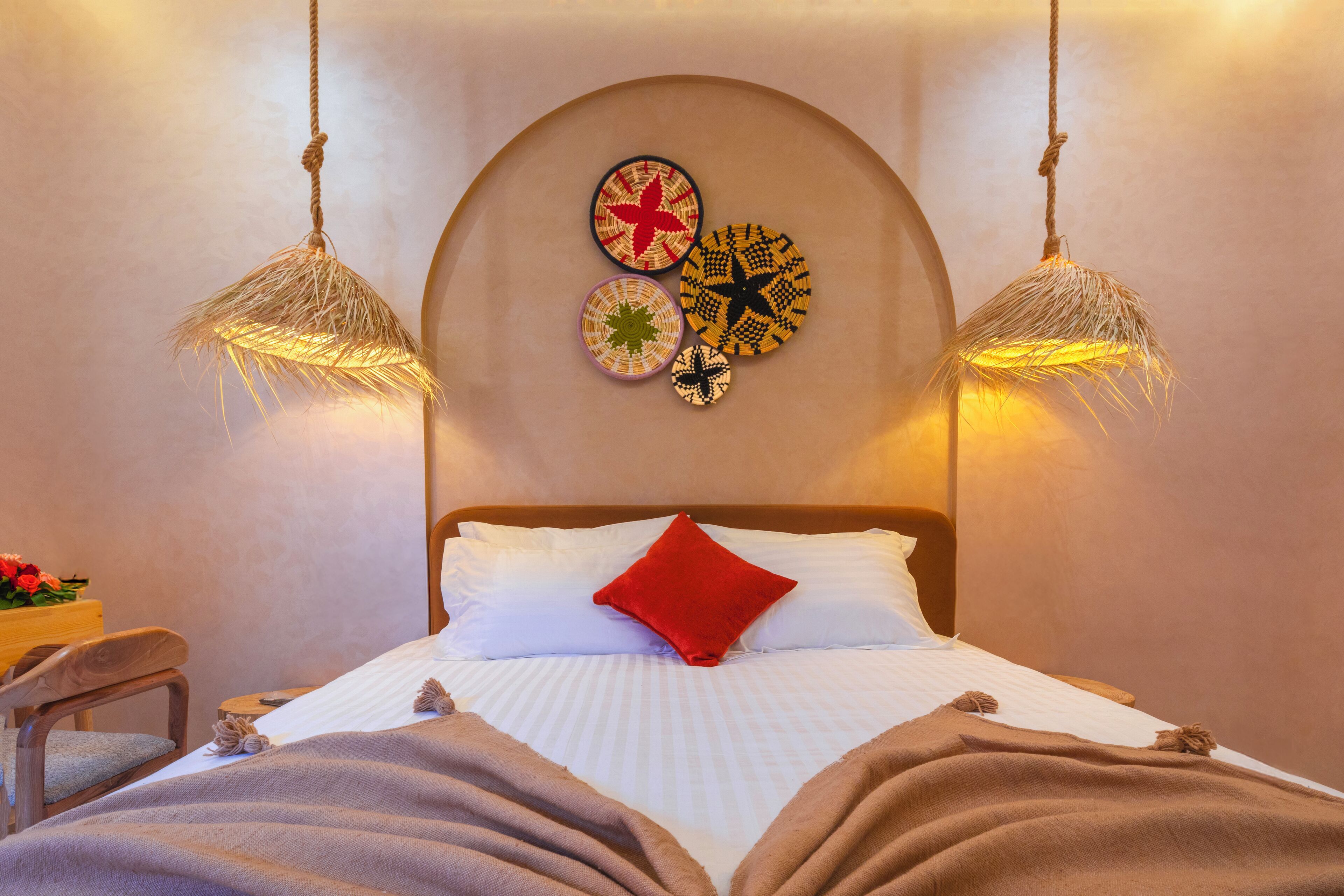 A neatly made bed with a red pillow, a headboard with wall art, and two hanging lamps.