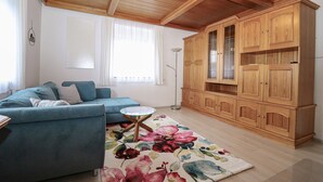 A living room with a blue sofa, a small round table, a floral rug, and wooden cabinets. - Lovely apartment in Strau with WiFi (Strau)