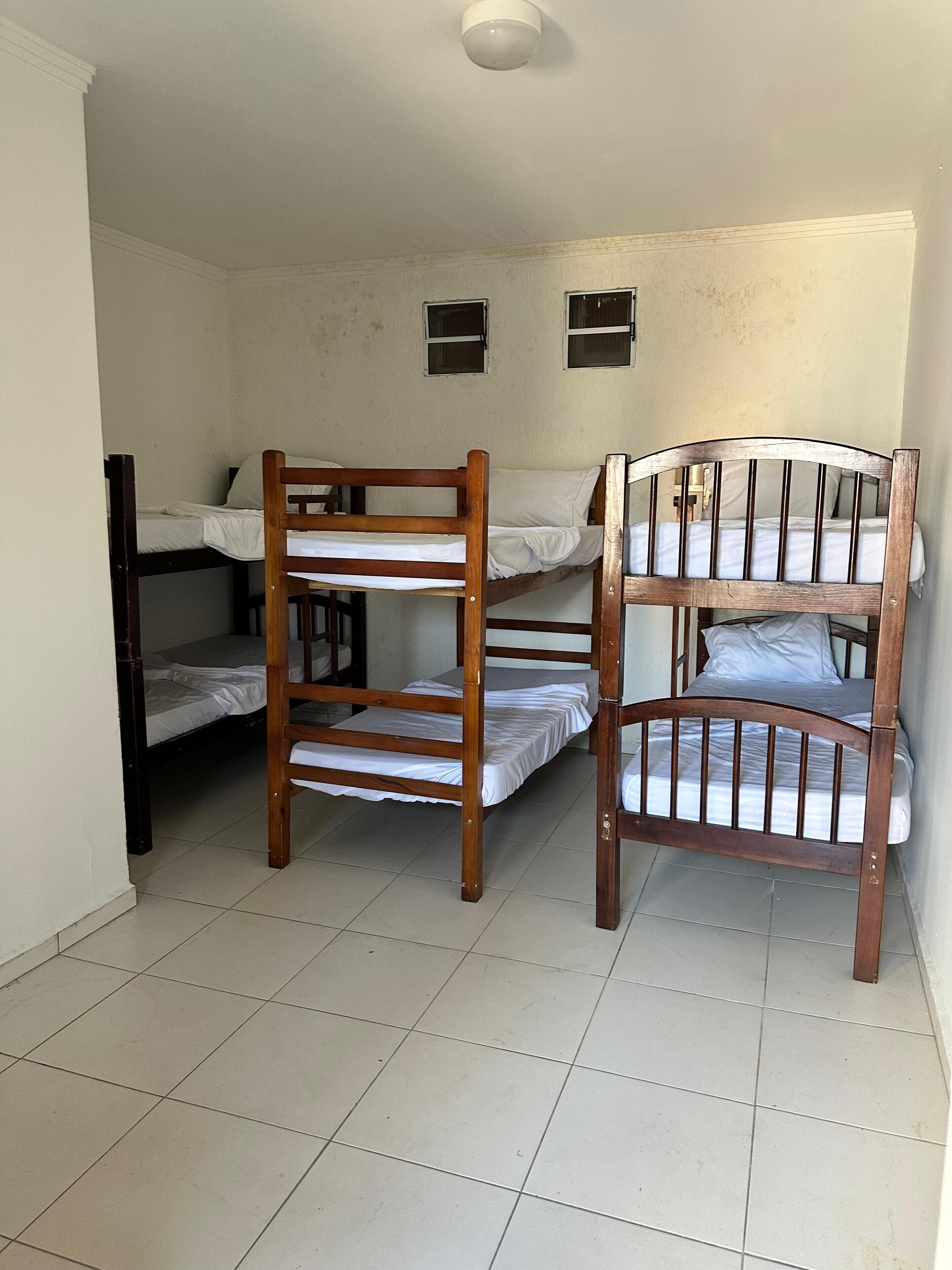 A dormitory room with two bunk beds, a small window, and a ceiling light.