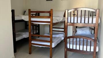 A dormitory room with two bunk beds, a small window, and a ceiling light.