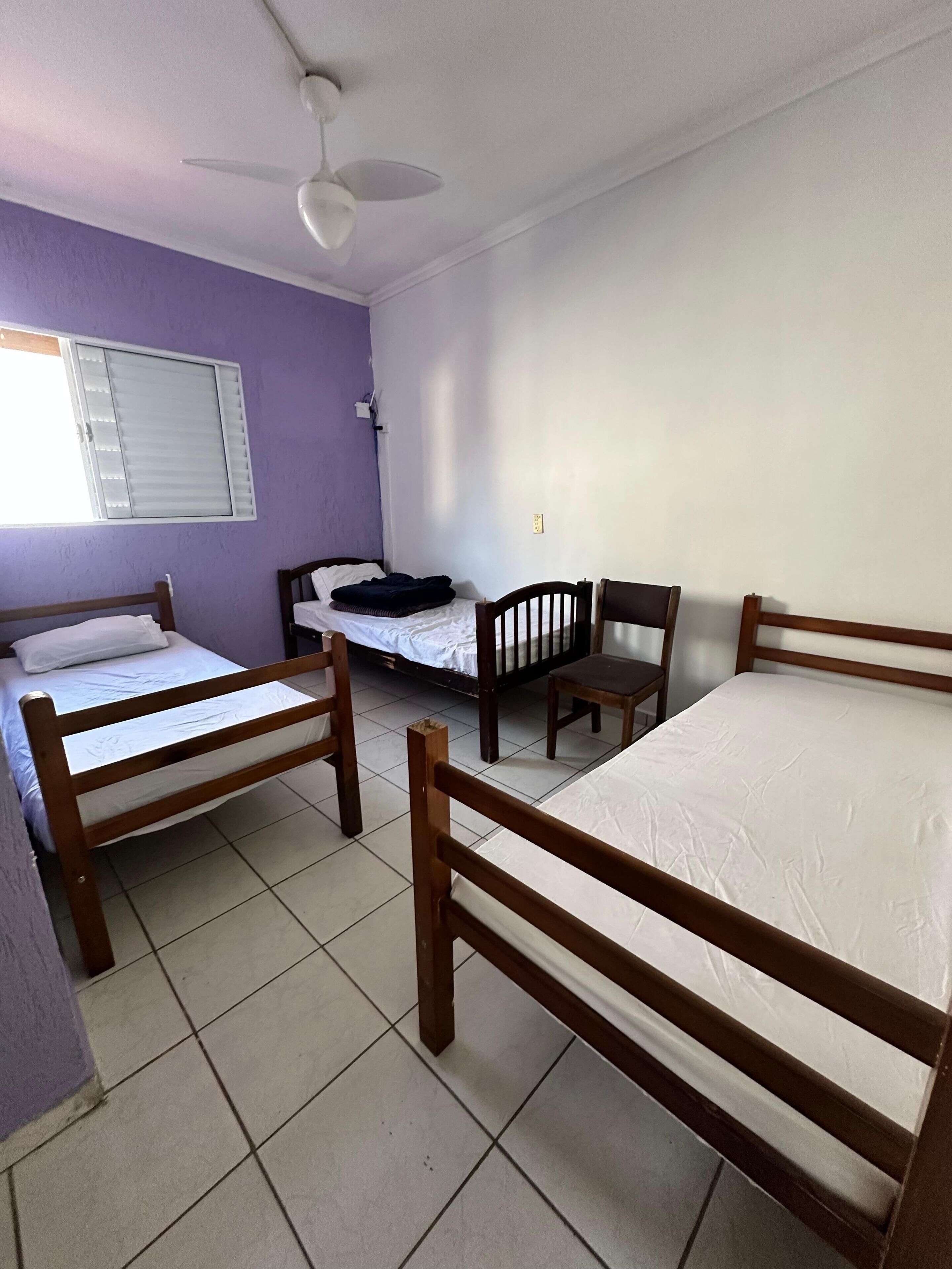 A dormitory room with three wooden bunk beds, a ceiling fan, and a window with blinds.