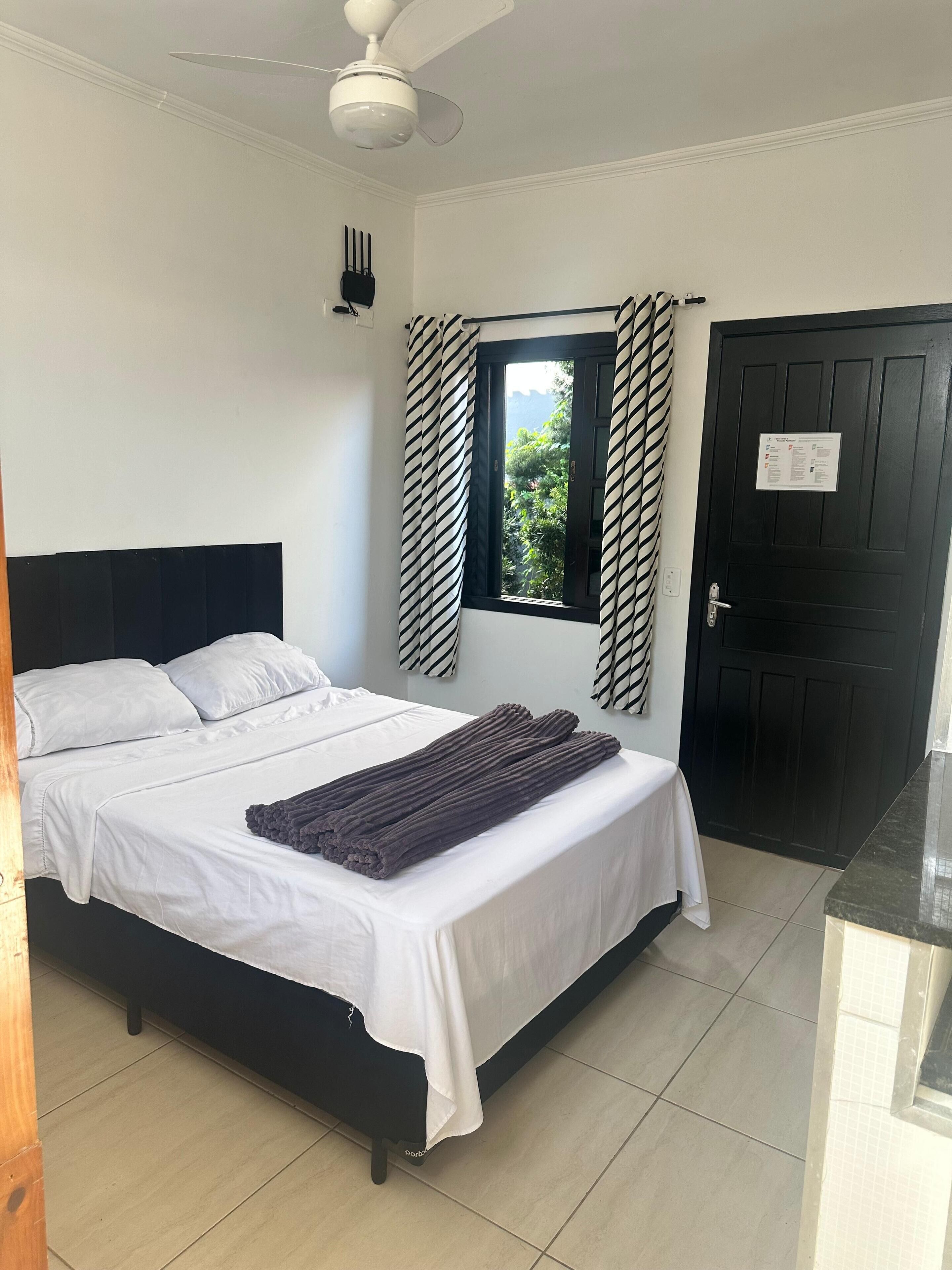 Un dormitorio con cama, ventana con cortinas, puerta y ventilador de techo.