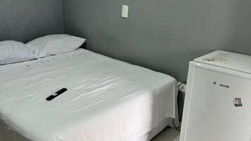 Una habitación con una cama, un refrigerador blanco y una pared gris.