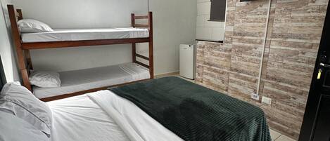 Una habitación con dos literas, un ventilador de techo, un televisor de pantalla plana montado en una pared con estampado de ladrillo y un refrigerador.