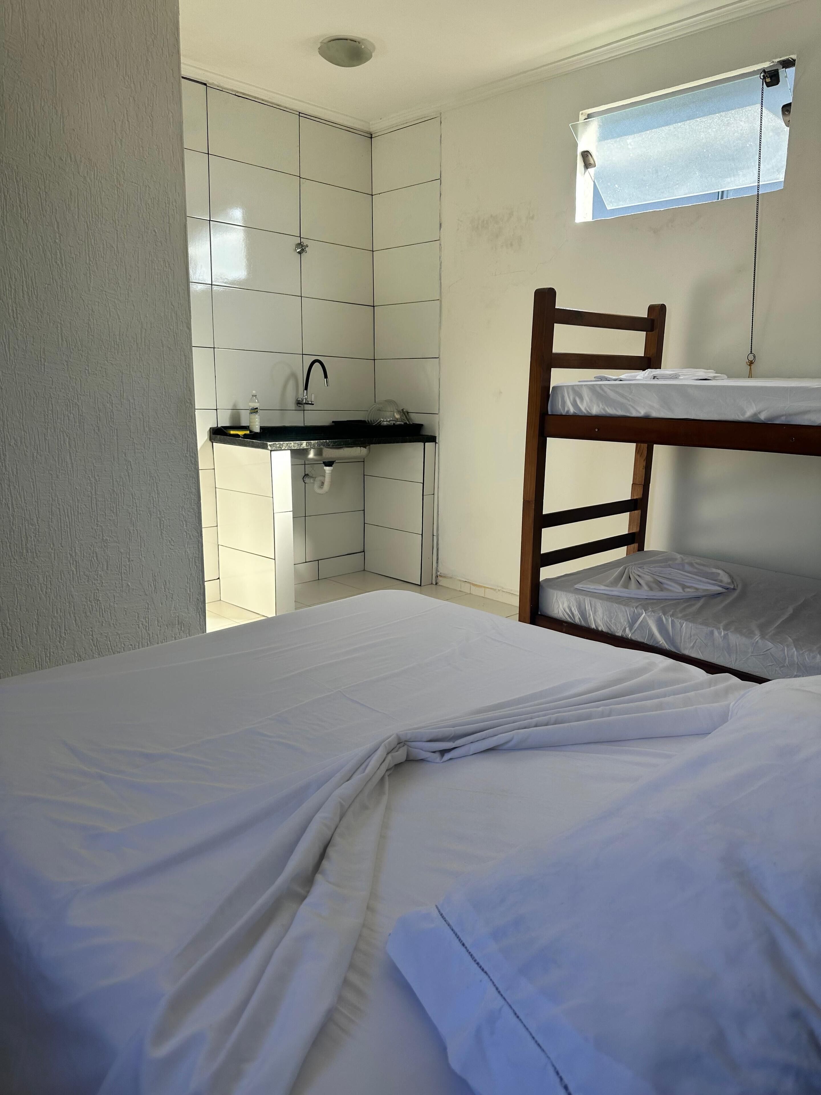 A small, compact room with a bunk bed, a kitchenette with a sink and a window above the bed.