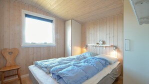 Ein Schlafzimmer mit Bett, Sessel, Fenster und einem an der Wand befestigten Regal mit einer Uhr.
