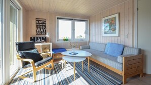 Ein gemütliches Zimmer mit Holzvertäfelung, einer Couch, einem Sessel, einem kleinen Tisch und einem Fenster.