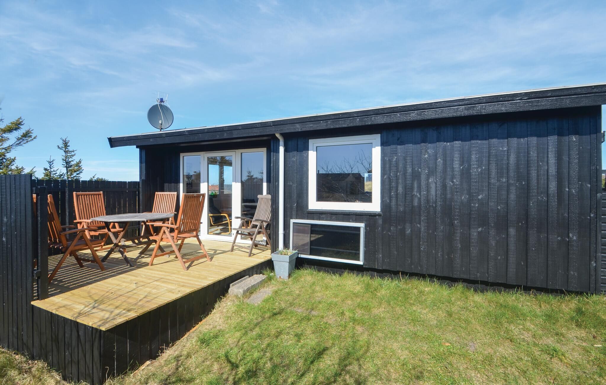 A modern, single-story cabin with a deck, outdoor seating, and a satellite dish.