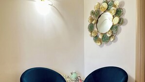 Et værelse med to blå lænestole, et lille bord med en lampe, et dekorativt spejl og en aircondition på væggen.