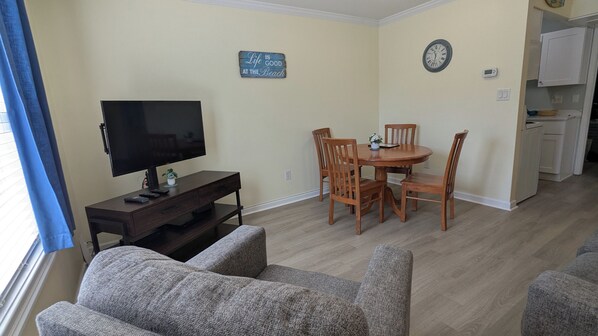 A living room with a TV, a dining table with chairs, a clock, and a sign on the wall.