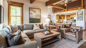 A spacious living room with a large sectional sofa, a coffee table, and a leather armchair. A kitchen with wooden cabinets and a dining area is visible in the background. - Stunning, Remodeled Mountain Retreat in Mammoth Lakes! (Mammoth Lakes)
