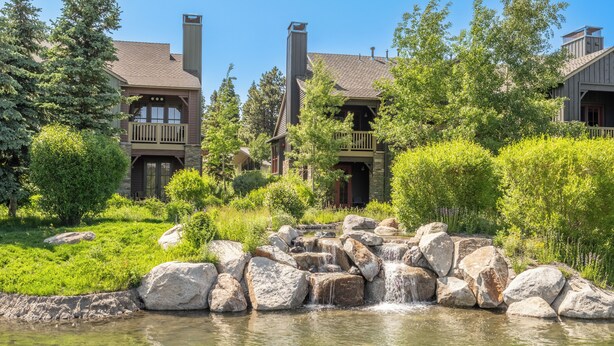 A lodge with a stone facade, multiple balconies, and a small waterfall feature in the foreground. - Stunning, Remodeled Mountain Retreat in Mammoth Lakes! (Mammoth Lakes)