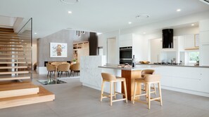 A modern kitchen with a central island, bar stools, a dining area with chairs, and a staircase.