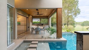 A modern outdoor kitchen with a dining area, a ceiling fan, and a pool. - ROSALIE ESTATE - THE VINTAGE HOLIDAY HOUSES (POKOLBIN)