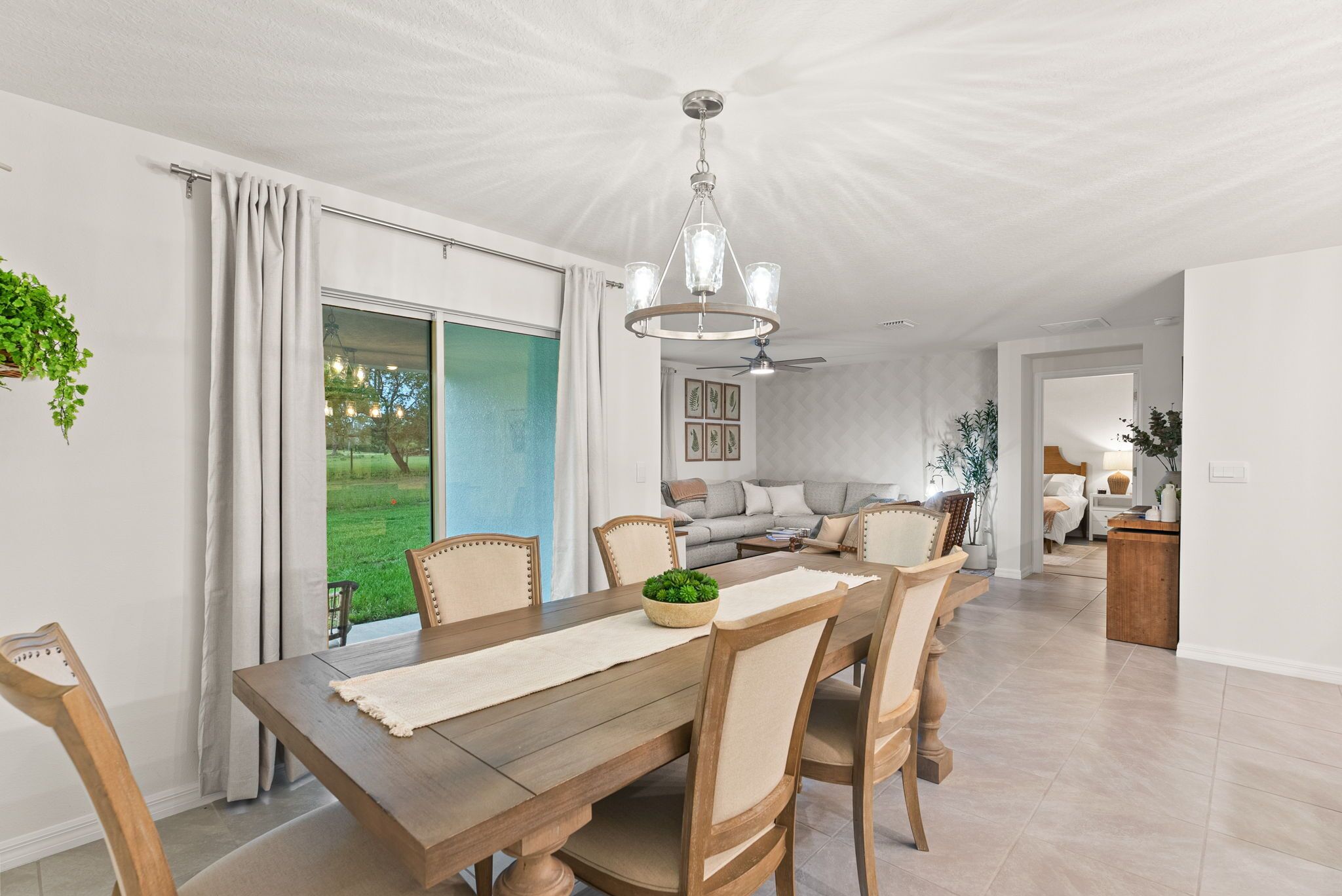 Un coin repas avec une table en bois, des chaises et un lustre. Une porte-fenêtre coulissante donne accès à un patio d’où l’on peut admirer une pelouse verdoyante.