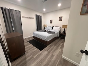 Une chambre à coucher comprenant un lit, des tables de chevet, une commode et une œuvre d’art accrochée au mur.