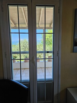 A sliding glass door leading to a balcony with potted plants and a view of the sky.