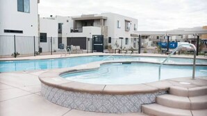 Une piscine avec un jacuzzi, entourée d’une clôture et bordée de bâtiments modernes en arrière-plan.