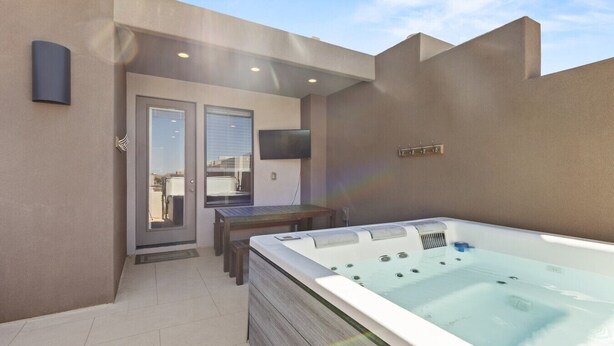 Une terrasse extérieure moderne dotée d’un jacuzzi, d’une table et d’une porte donnant sur un espace abrité.