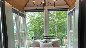 A bedroom with a large bed, two bedside lamps, and a view of trees through large windows.
