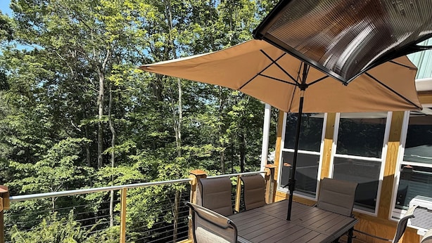 A deck with a table and chairs, surrounded by a wooden railing, overlooking a forested area.