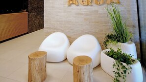 A reception area with a wooden ceiling, a stone wall, and a sign reading "POLANKI AGUA". There are three white, modern seating areas and two wooden stools.