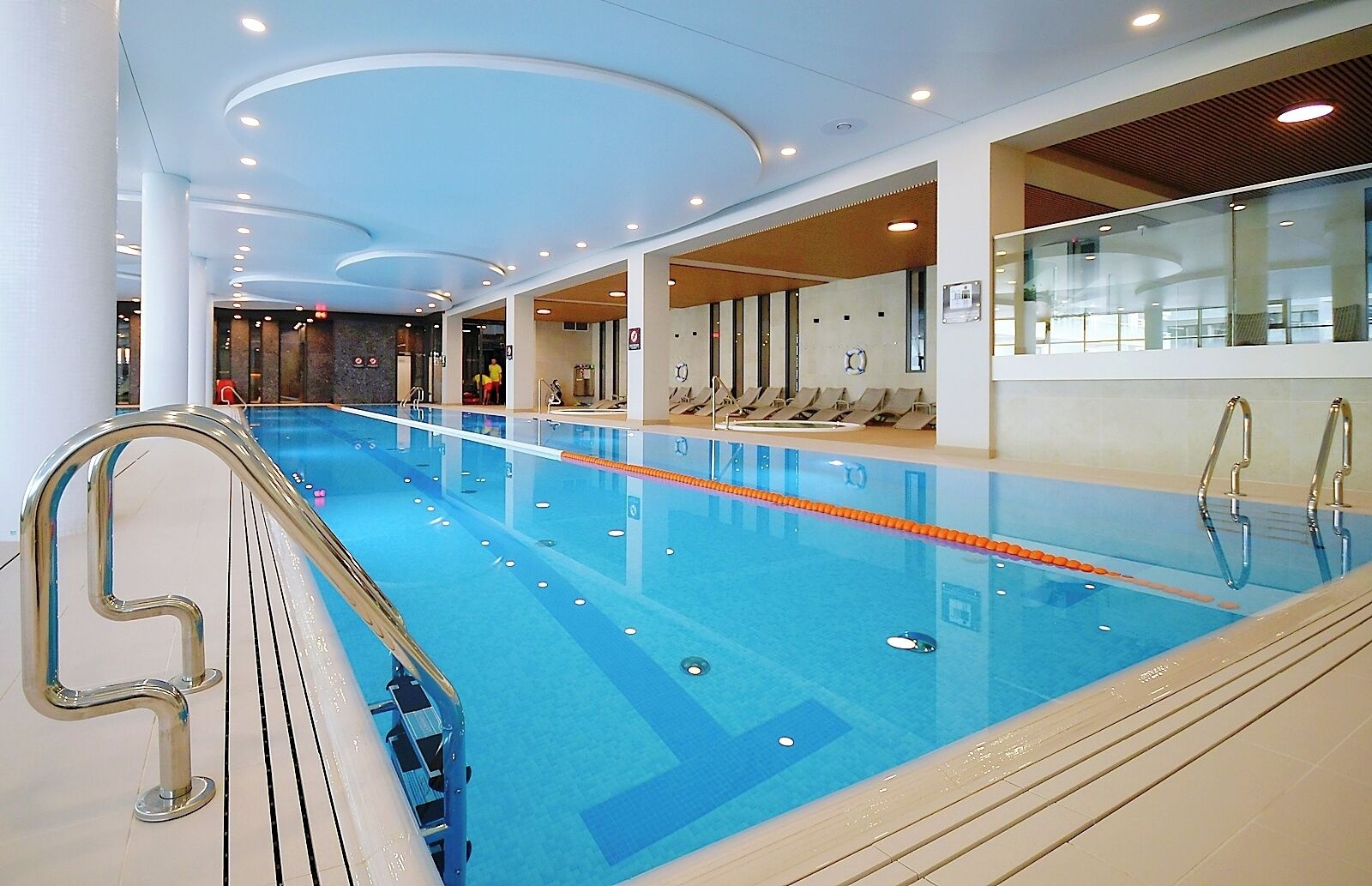 Una piscina interior con carriles delimitados, una escalera metálica e iluminación empotrada en el techo.