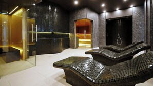 A modern spa area with a glass enclosure, a wooden sauna, and a black wall with a hanging ring.
