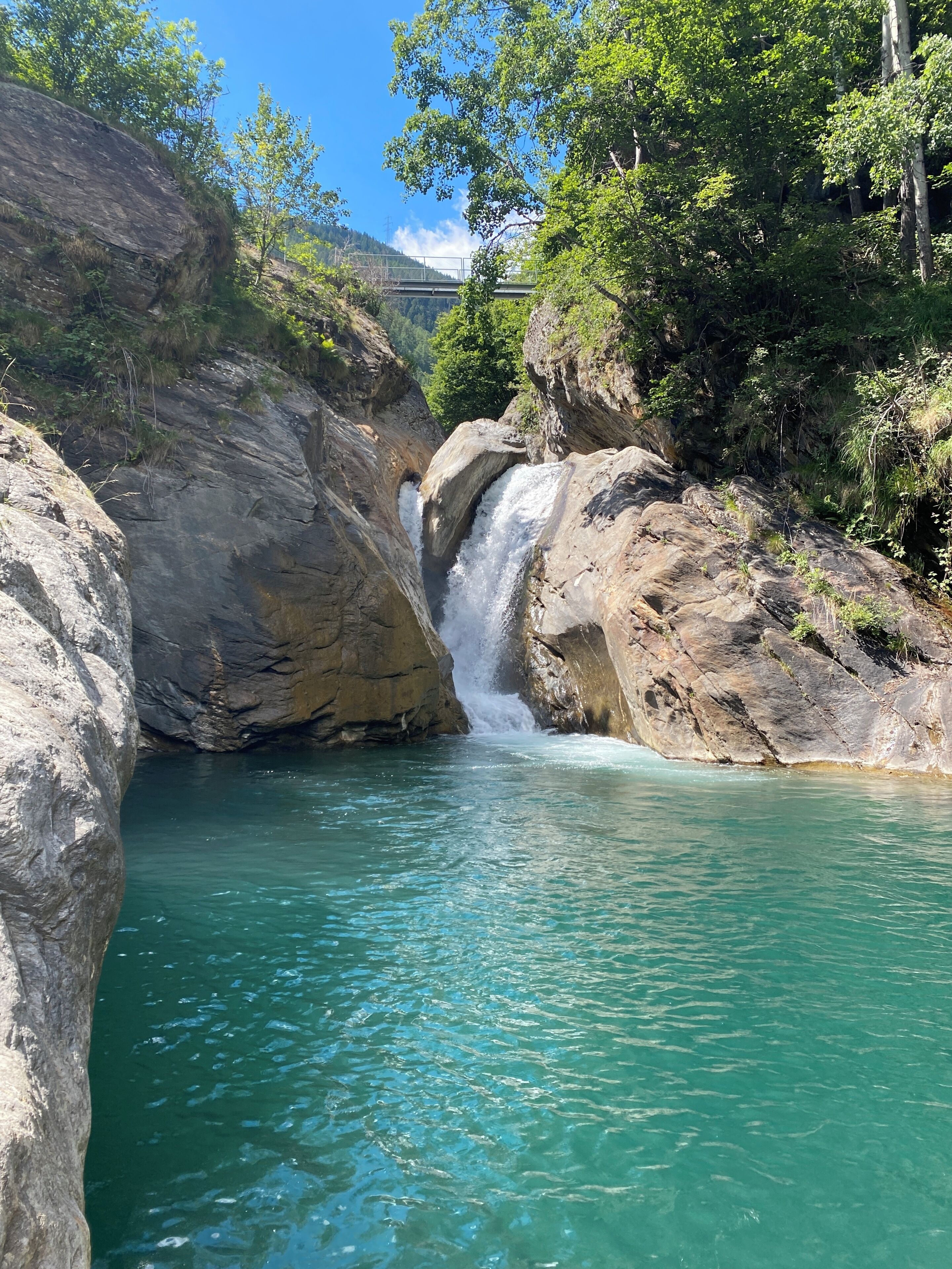 Una cascata naturale circondata da terreno roccioso e vegetazione.