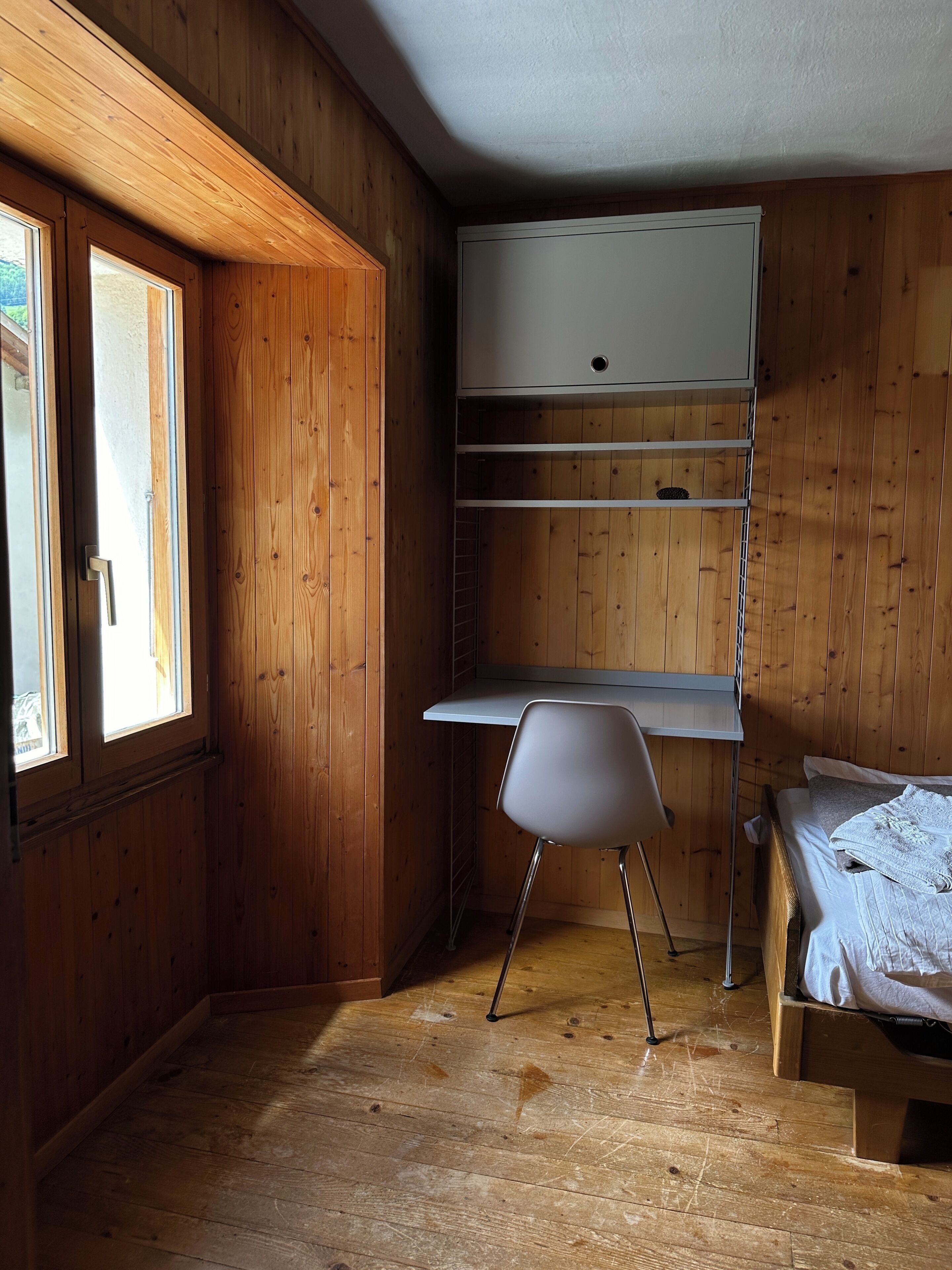 A room with wooden walls, a bunk bed, a desk with a chair, and a window.