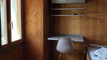 A room with wooden walls, a bunk bed, a desk with a chair, and a window.