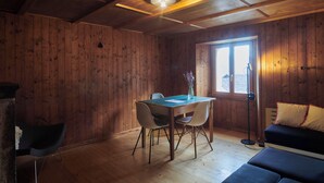 A wooden-paneled room with a dining table, two chairs, a sofa, and a window.