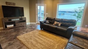 Ein Wohnzimmer mit einem großen Flachbildfernseher, einem Ledersofa und Seeblick.