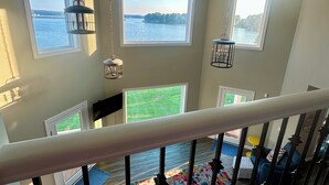 Ein geräumiges Zimmer mit großen Fenstern und Blick auf ein Gewässer, ein Balkon mit Geländer und eine Aussicht auf eine Wiese.