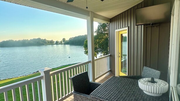 Eine überdachte Terrasse mit Korbmöbeln, einem Deckenventilator und Blick auf einen See.