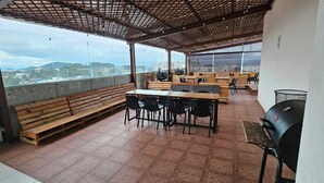 Une terrasse extérieure avec des bancs et des tables en bois, un barbecue et une vue sur la ville.