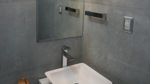 Un baño moderno con un lavamanos blanco, un espejo grande y una lámpara de pared.