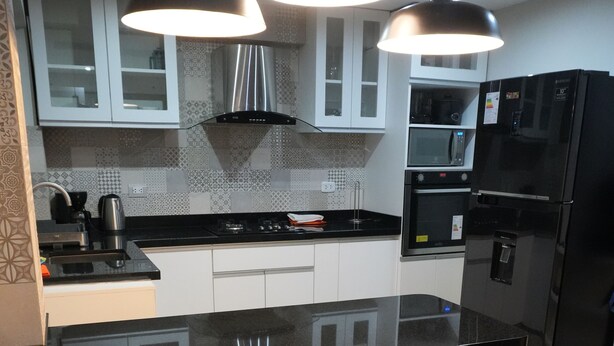 Una cocina moderna con encimera negra, dos taburetes de madera e iluminación colgante.
