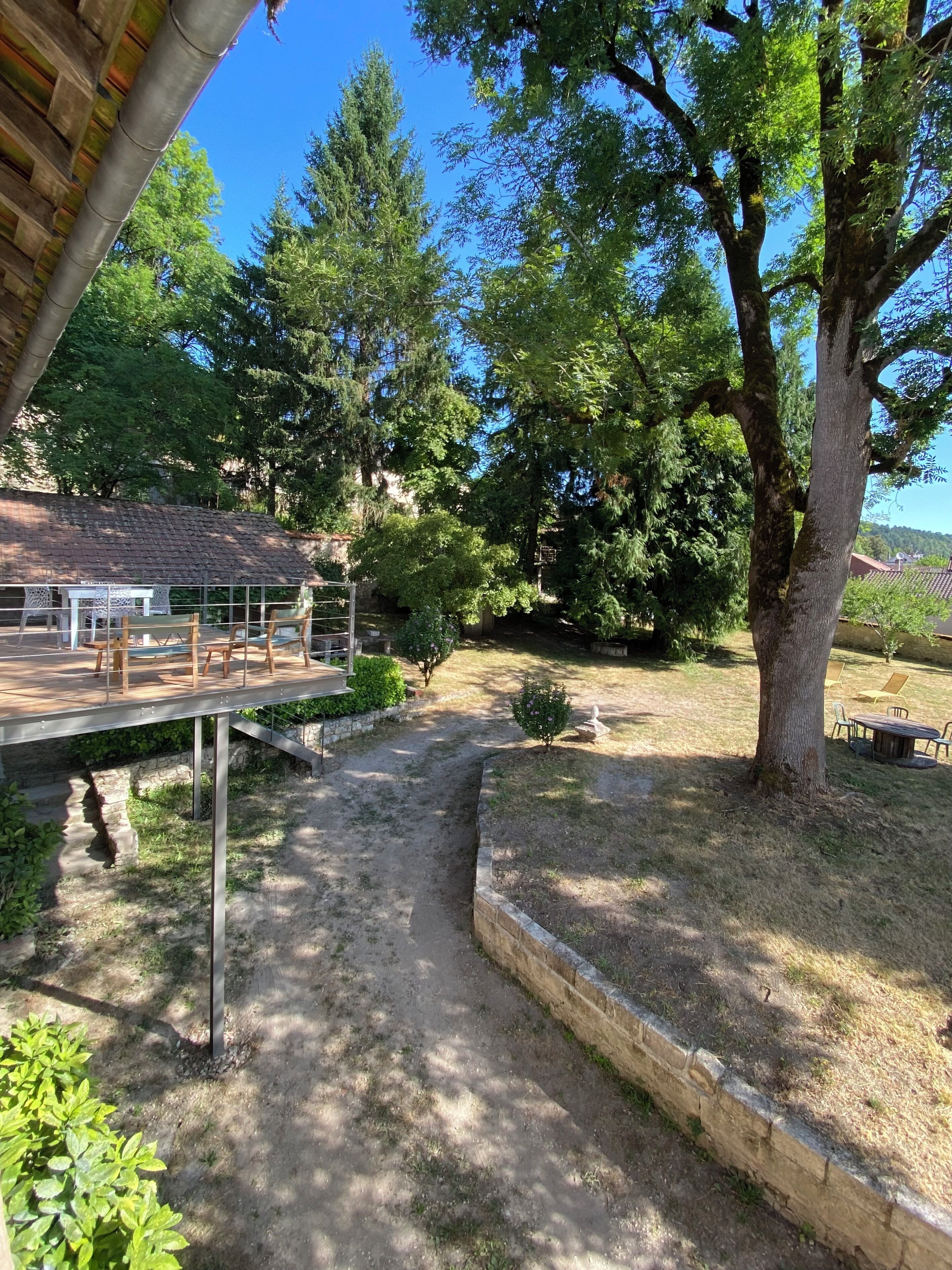 A covered outdoor area with a wooden deck, surrounded by trees and a stone wall.