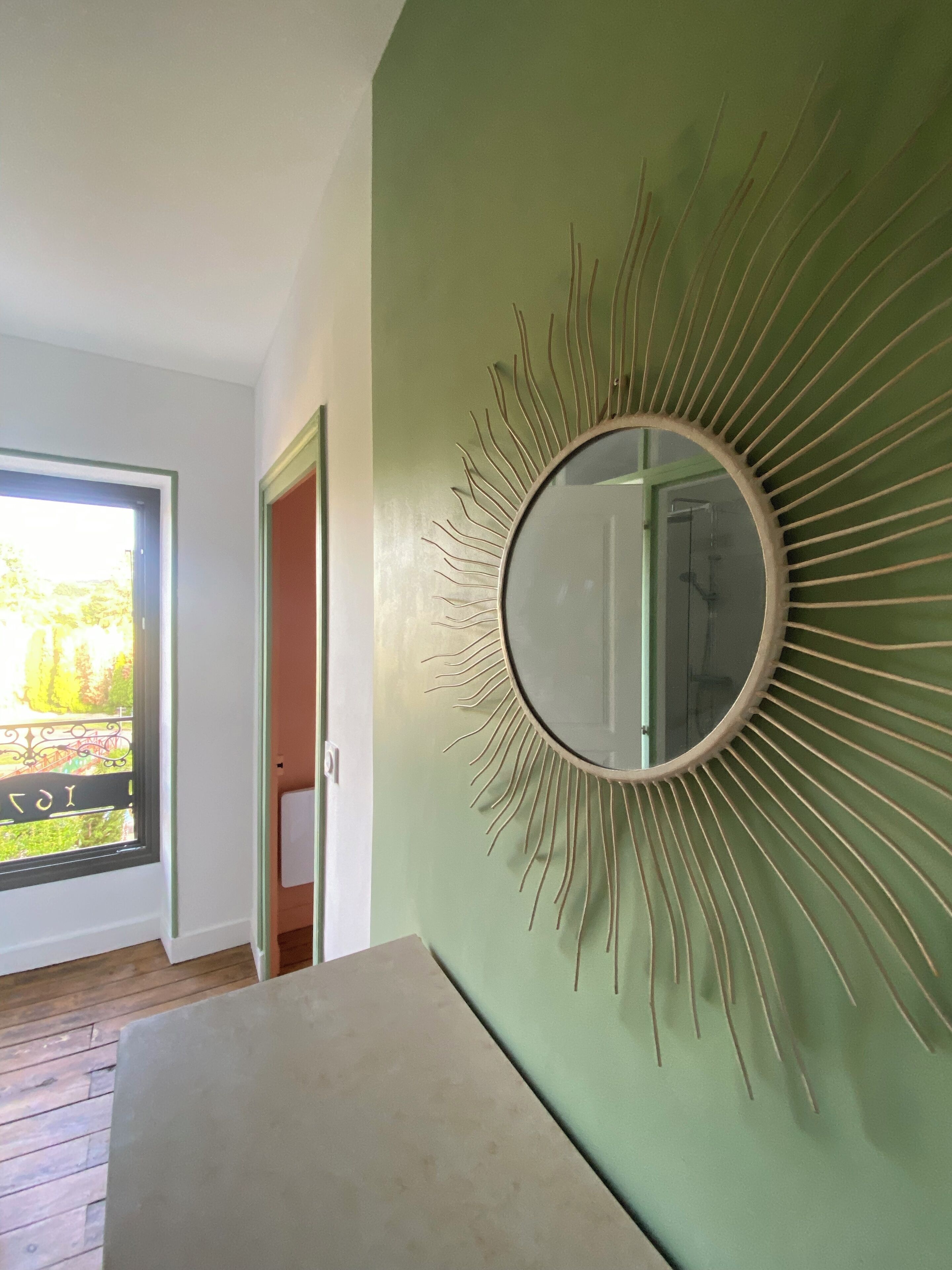 A room with a large mirror on a green wall, wooden flooring, and a door leading outside.