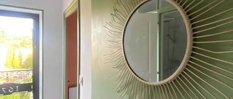 A room with a large mirror on a green wall, wooden flooring, and a door leading outside.