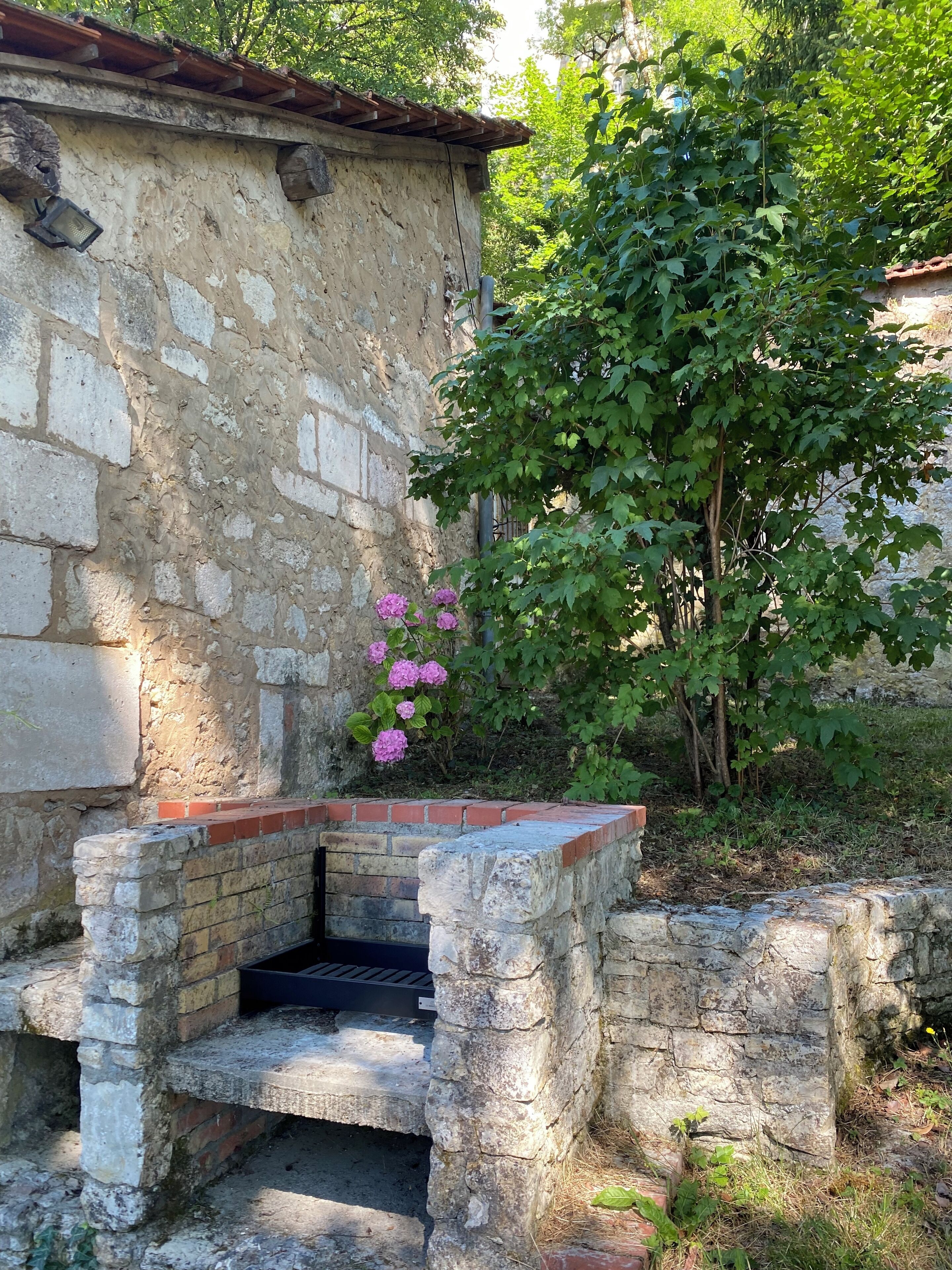 Een rustiek stenen gebouw met een bakstenen bankje en een kleine tuin met roze bloemen.