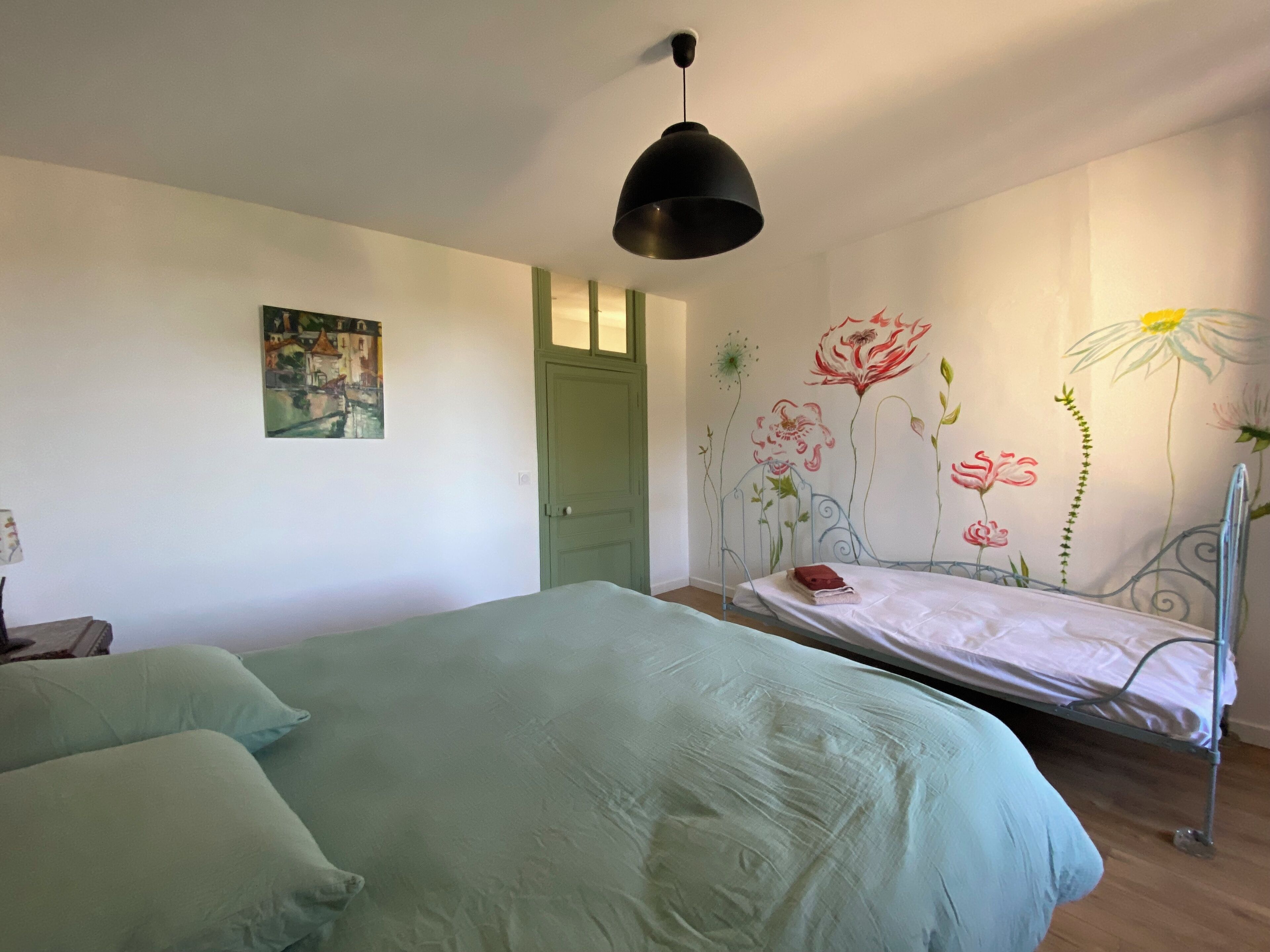 Een slaapkamer met een bed, een groene deur, een schilderij en een bloemen behang.