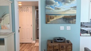 A room with a wooden floor, a white dresser, a painting of a beach scene, and a door leading to another room. - Directly on the beach at The Estero Beach and Tennis club. Balcony on the Ocean! (Fort Myers Beach)
