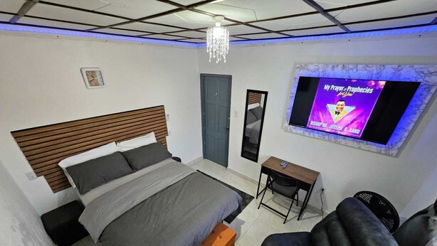 A bedroom with a bed, a desk, a chair, a TV, and a chandelier.