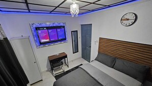 A modern bedroom with a bed, a desk, a wall-mounted TV, and a clock.