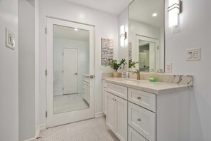 A modern bathroom with a large mirror, white cabinetry, and a tiled floor. - La Costa Comfort - Resort-style Living for 2 (Carlsbad)