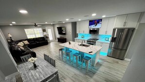 A modern kitchen with a central island, stainless steel appliances, and a flat-screen TV mounted above the island.