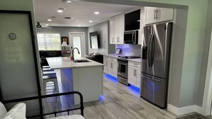 A modern kitchen with a central island, stainless steel appliances, and a dining area with a sofa.