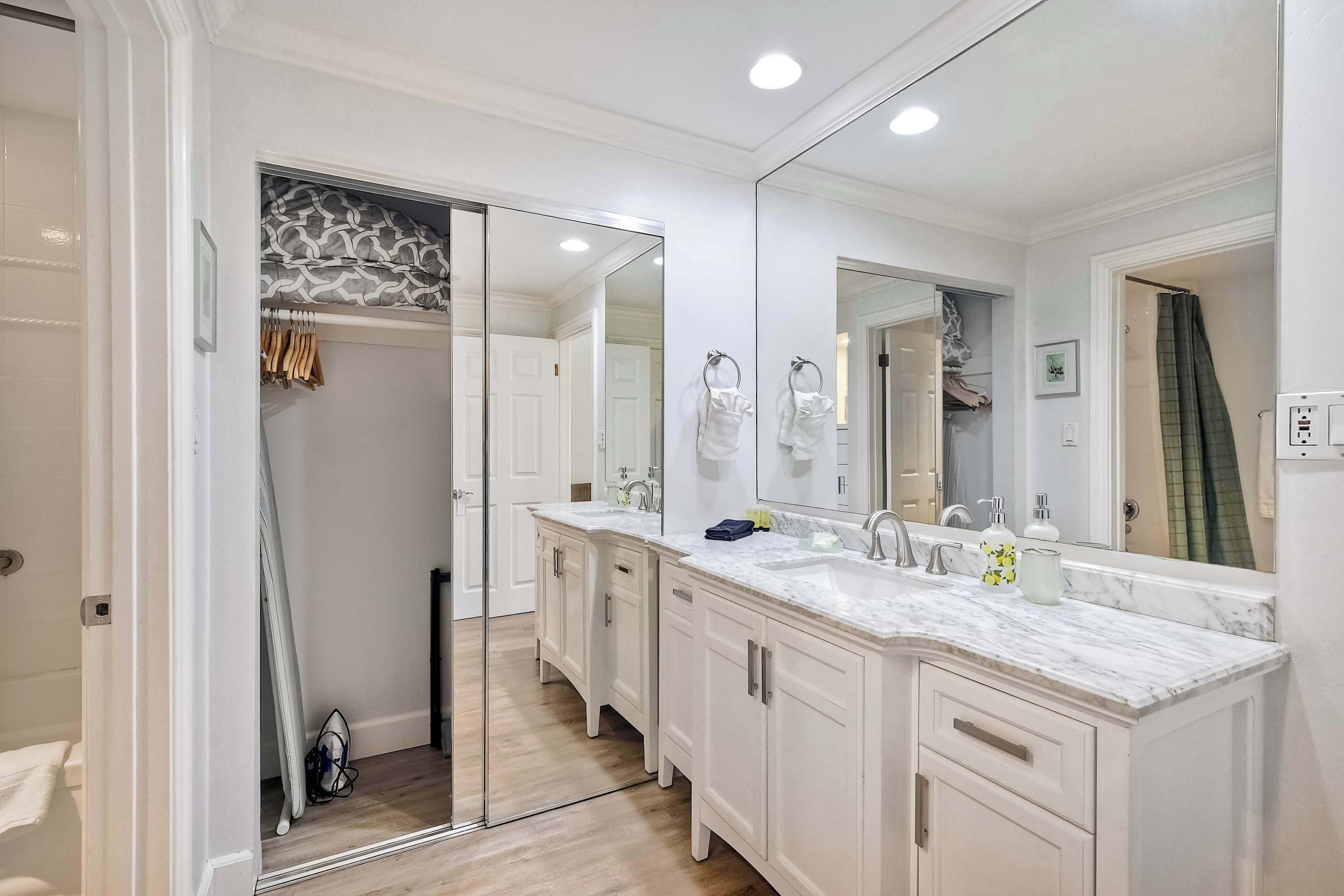 A bathroom with a large mirror, two sinks, and a walk-in closet.